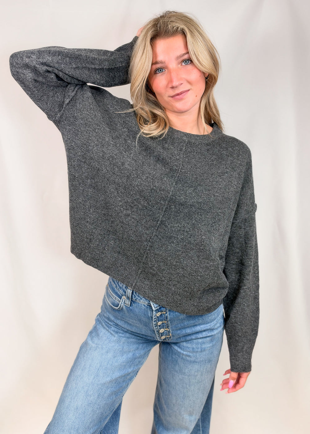 Woman wearing charcoal grey seamed sweater with jeans on plain background