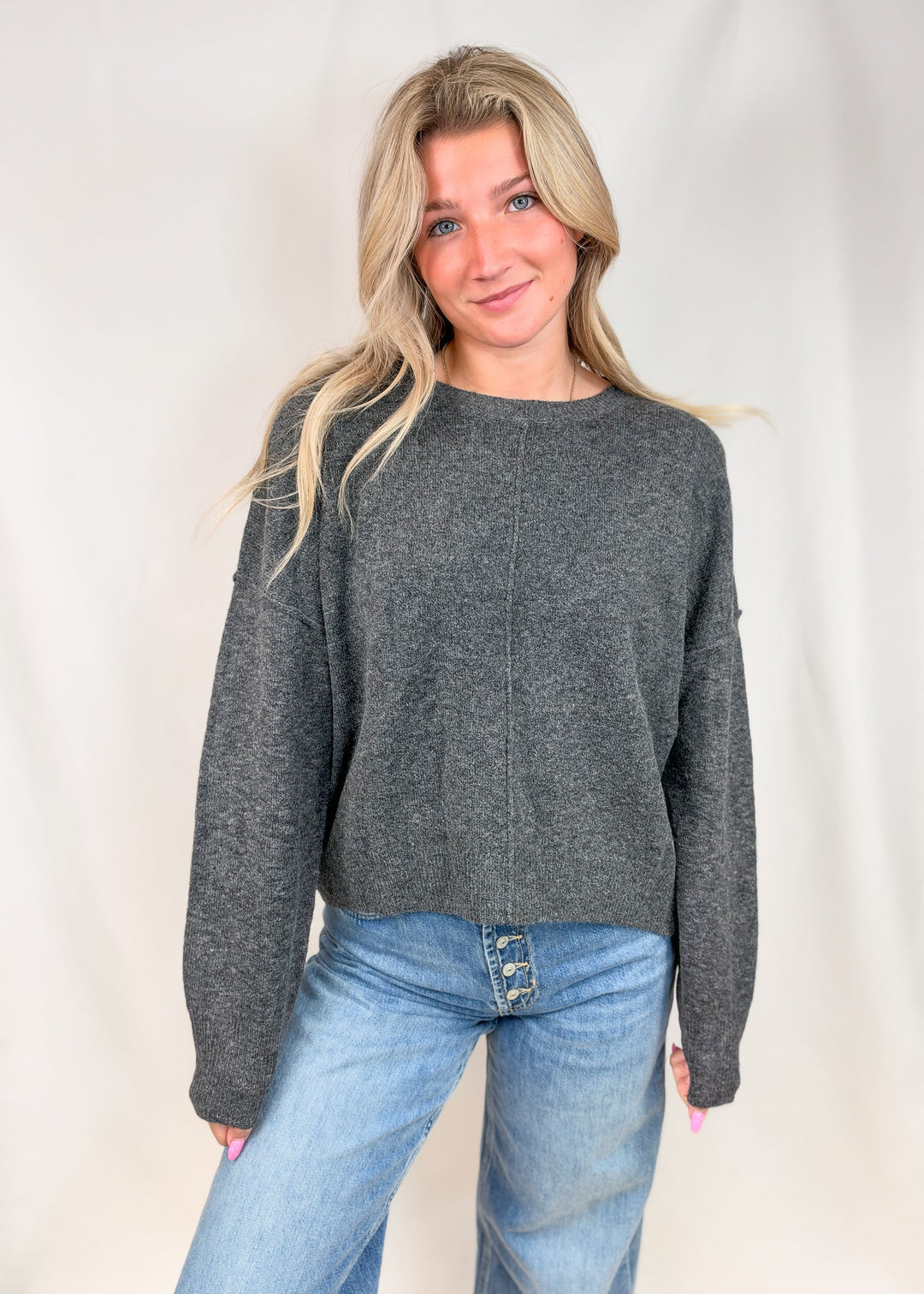 Woman wearing charcoal grey seamed sweater with jeans on plain background
