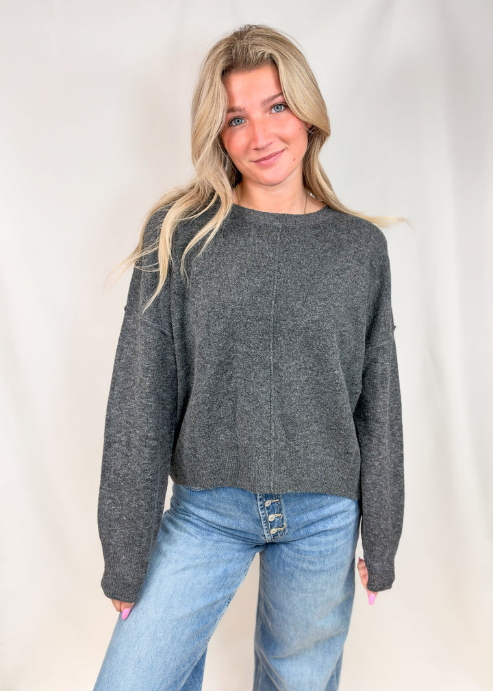 Woman wearing charcoal grey seamed sweater with jeans on plain background