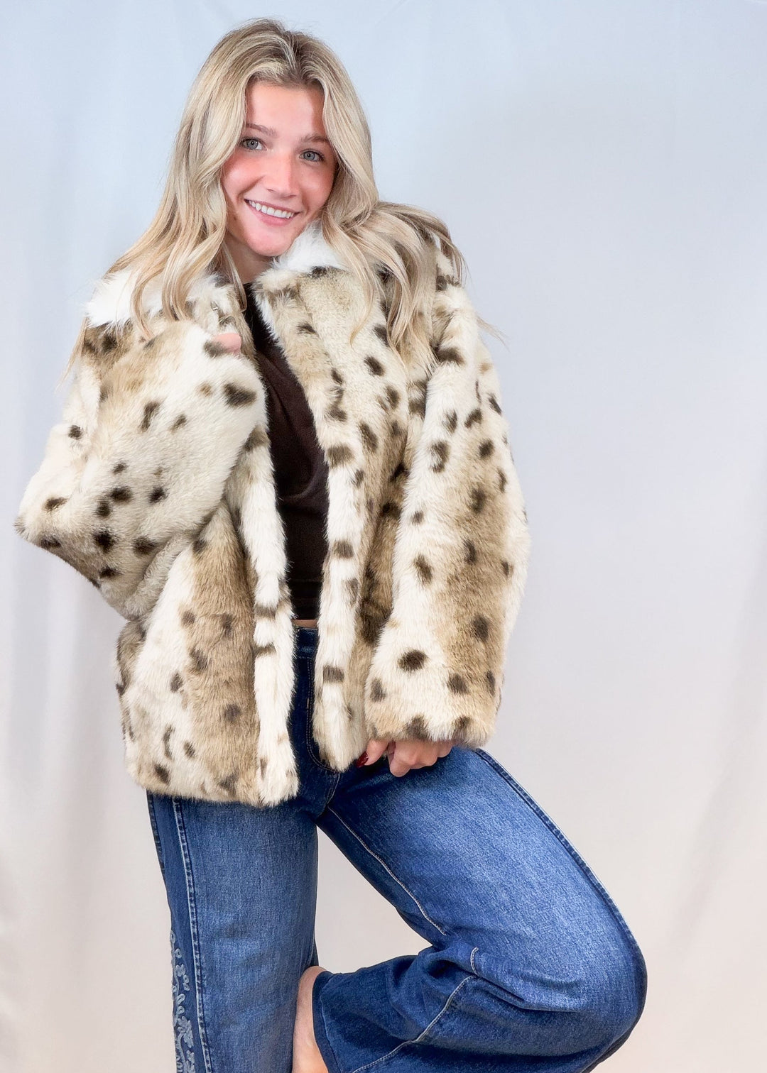 Woman wearing faux fur jacket with animal print and denim jeans on plain background