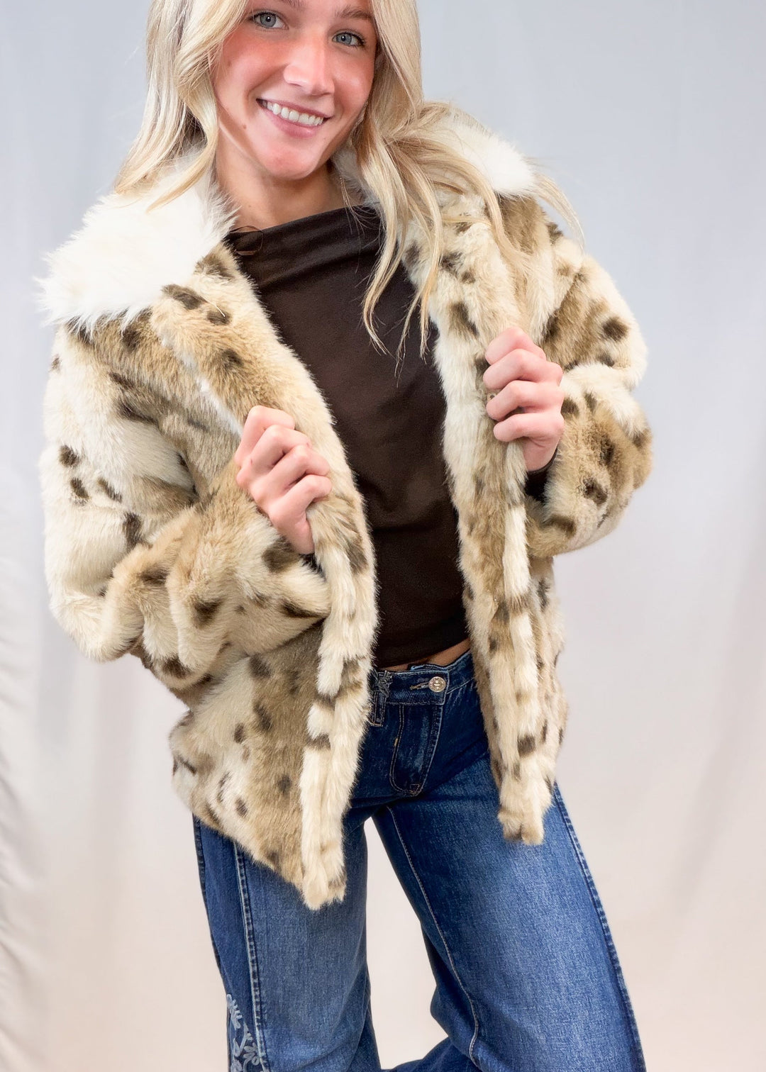 Woman wearing faux fur animal print jacket with denim jeans on plain background