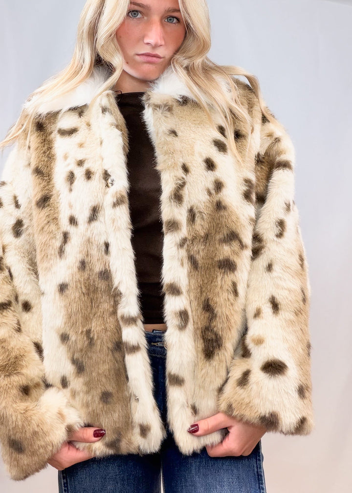Woman wearing faux fur animal print jacket with denim jeans on plain background
