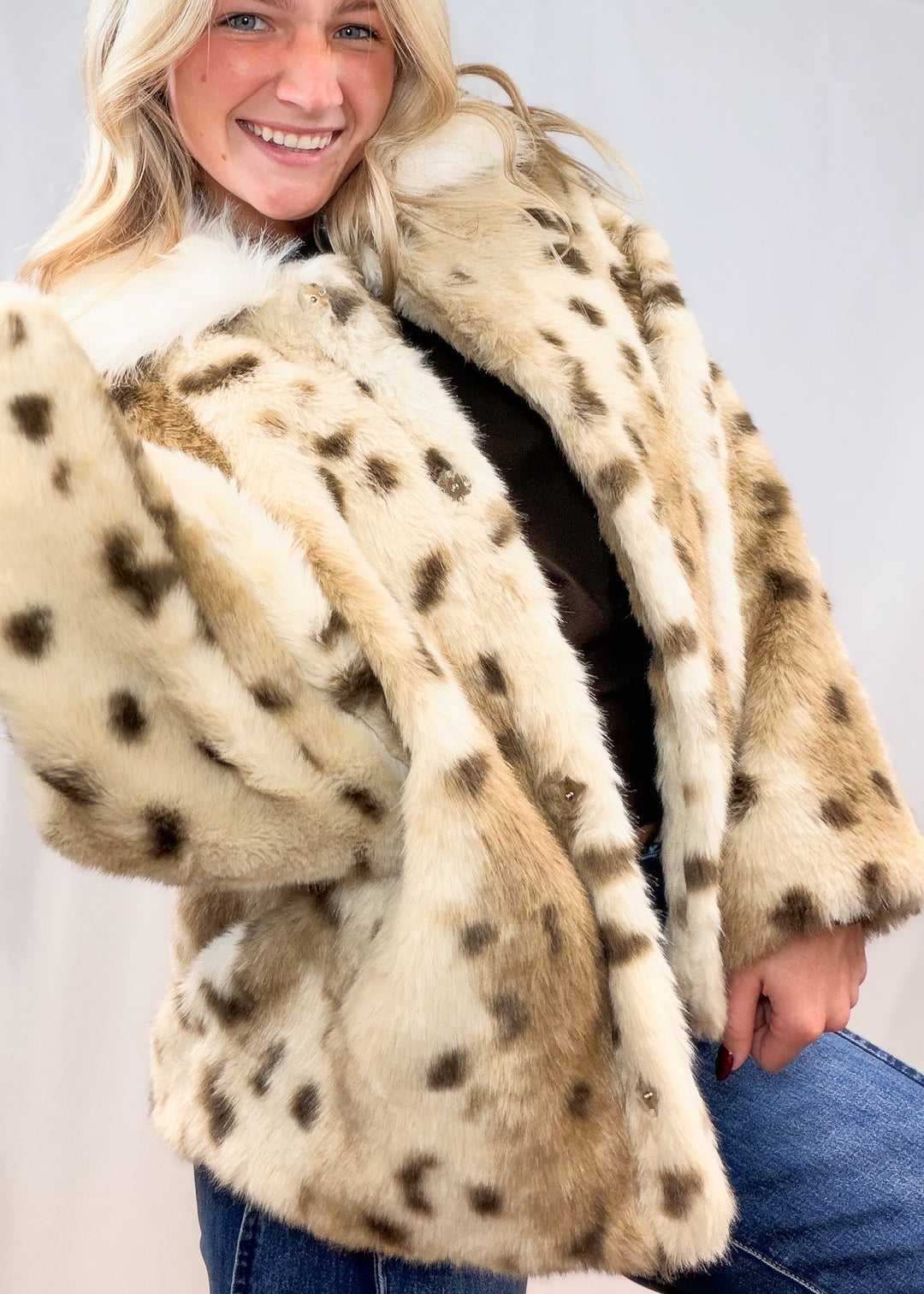 Woman wearing faux fur animal print jacket with denim jeans on plain background