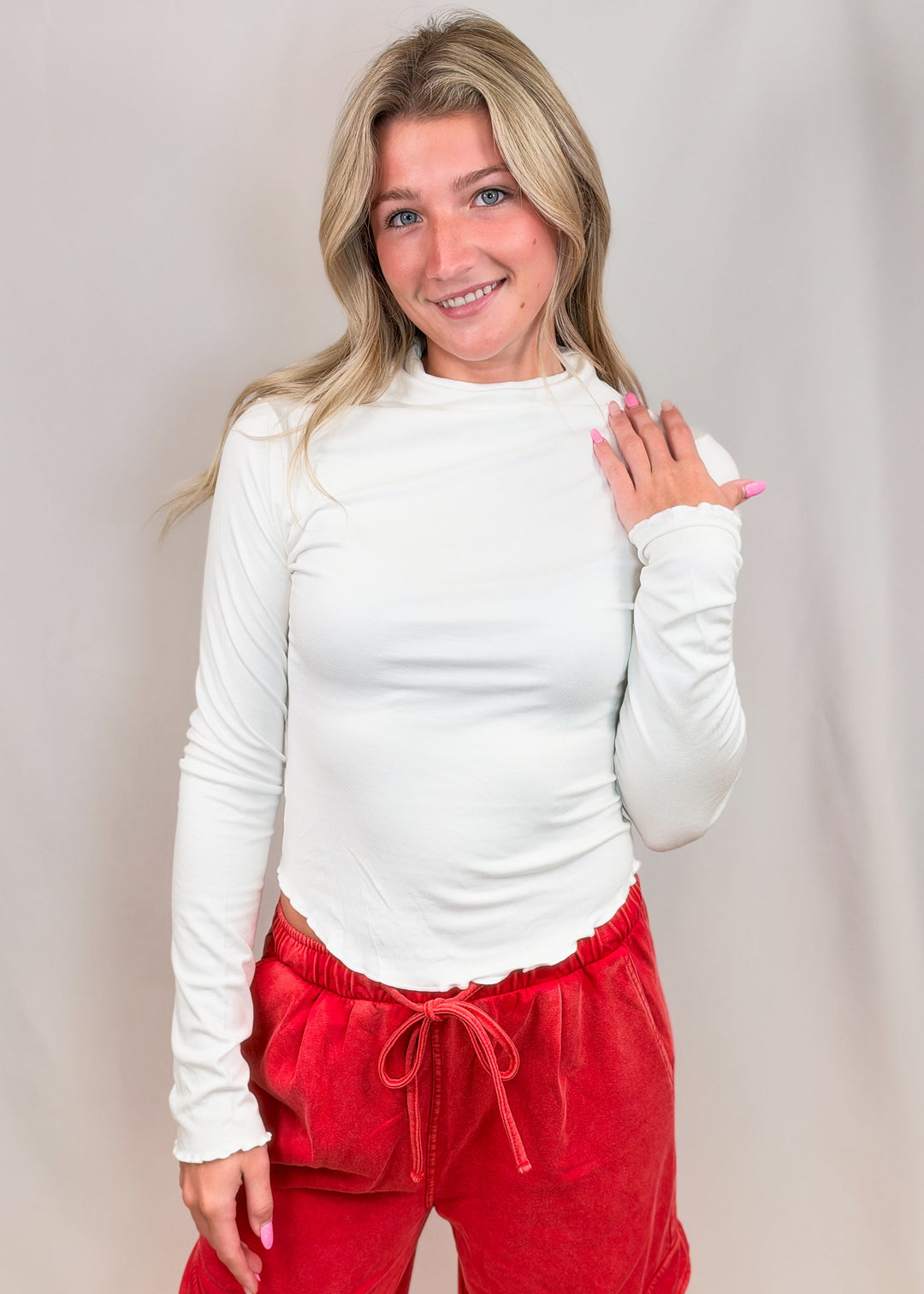 Woman wearing white top with lettuce detail edges and red pants on plain background