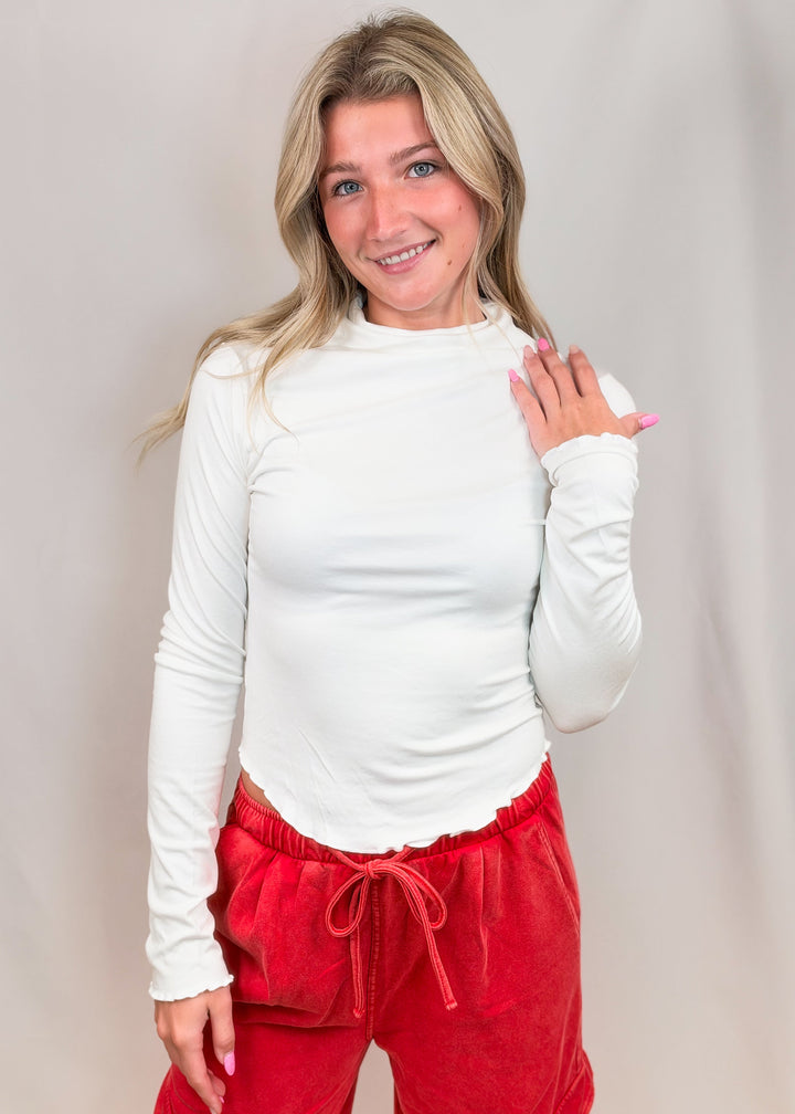 Woman wearing white top with lettuce detail edges and red pants on plain background