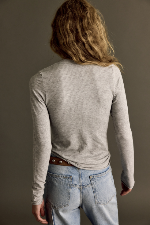 Woman shown from behind wearing long sleeve heather grey top and jeans on plain background