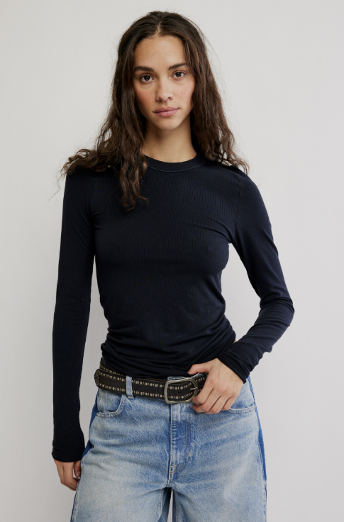 Woman wearing long sleeve ribbed black shirt and jeans on plain background