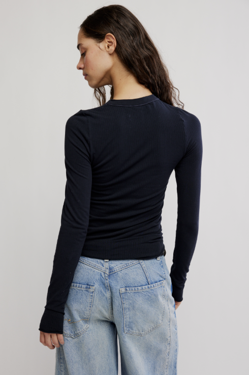 Woman shown from behind wearing long sleeve ribbed black shirt and jeans on plain background