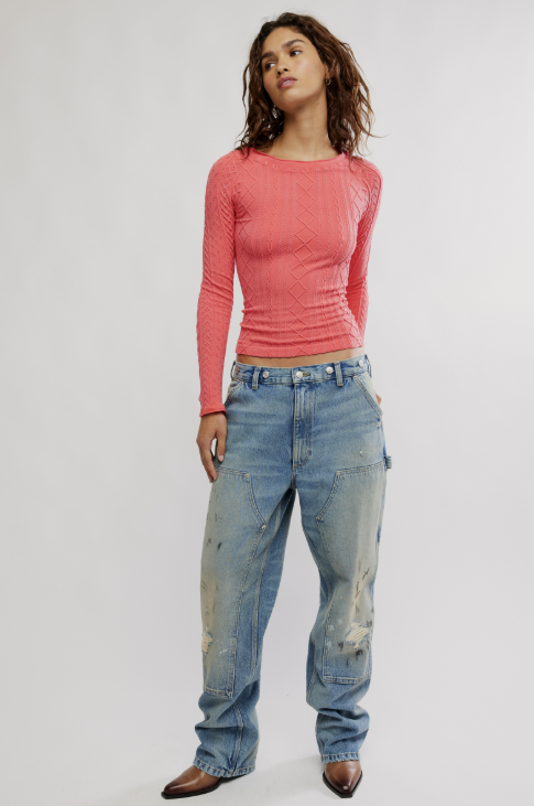Woman modeling coral long sleeve shirt with cable knit texture and jeans on white background