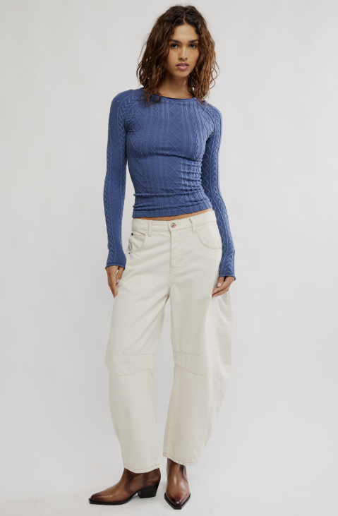 A model wearing a textured blue long-sleeve knit top and off-white wide-leg cropped pants, standing against a light gray studio background.