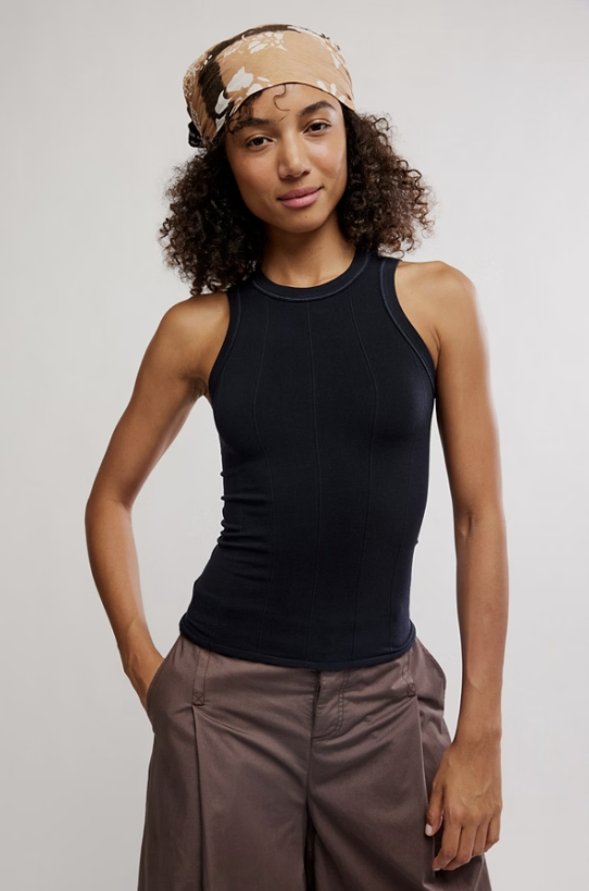 Woman wearing a black tank top and brown pants with a beige headband on a plain background