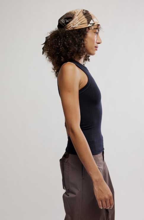 Woman wearing a black tank top and brown pants against a plain background