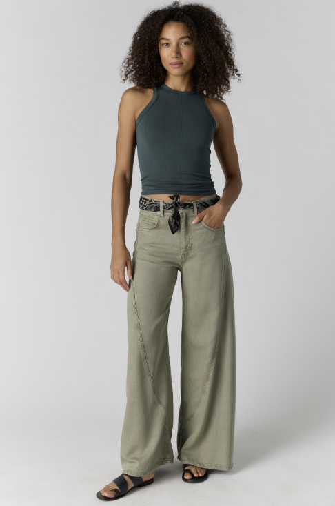 Woman wearing a green tank top and beige wide-leg pants on a white background