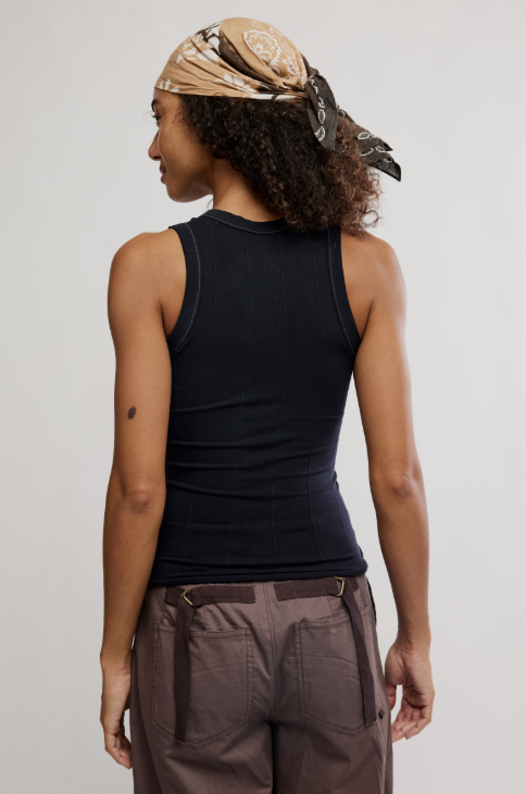 Person wearing a black tank top and brown pants with a beige headscarf.