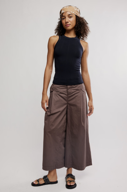 Woman wearing a black sleeveless top and brown wide-leg pants on a white background