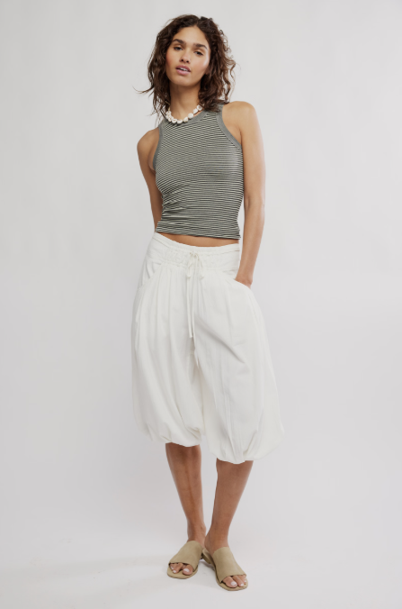 Woman wearing black and white stripe tank and white pants on plain background