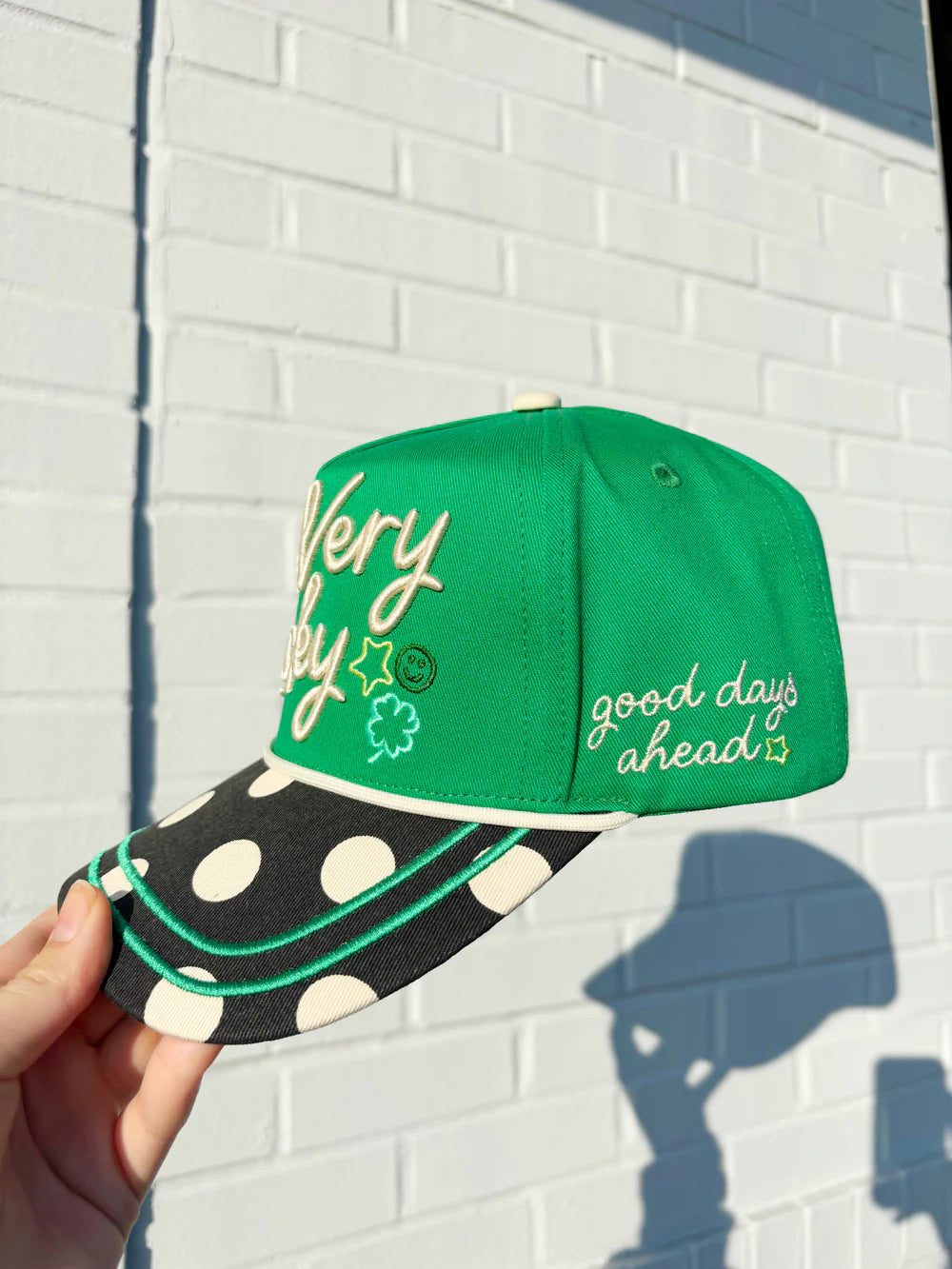 Green cap with polka dot brim held against a white brick wall