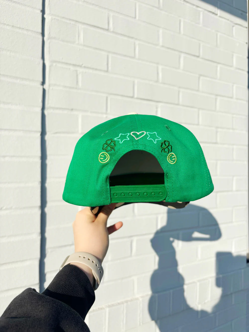 Green cap with star and heart designs held against a white brick wall