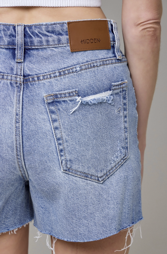 Close-up of a person wearing blue denim shorts with a &