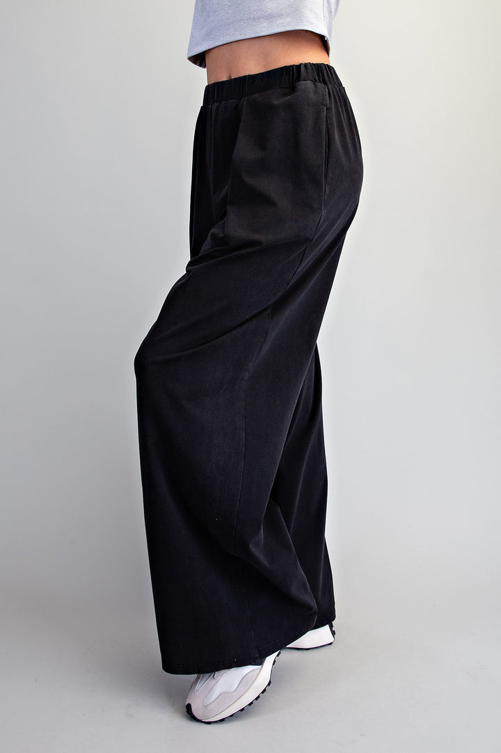 Black wide-leg pants with an elastic waistband, shown on a model from the waist down wearing white sneakers against a light gray background.