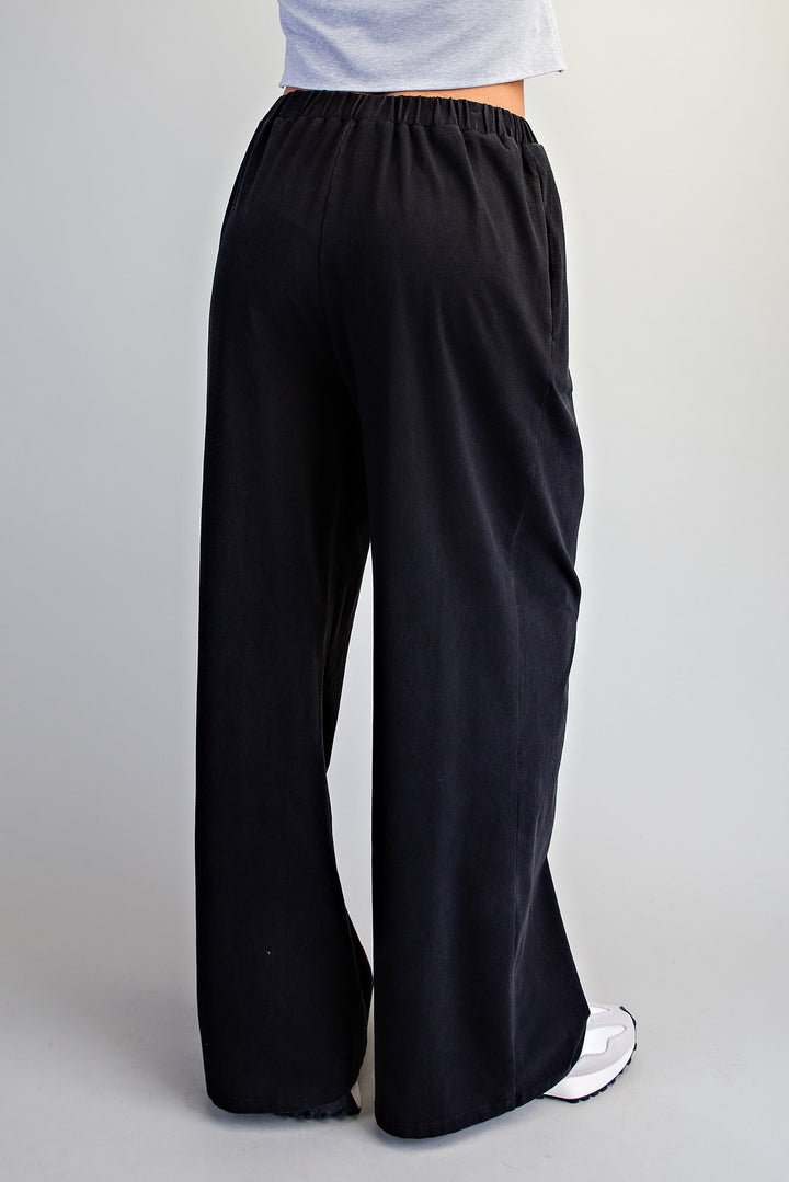 Black wide-leg pants with an elastic waistband, shown from the back on a model wearing a light gray top and white sneakers against a light gray background.