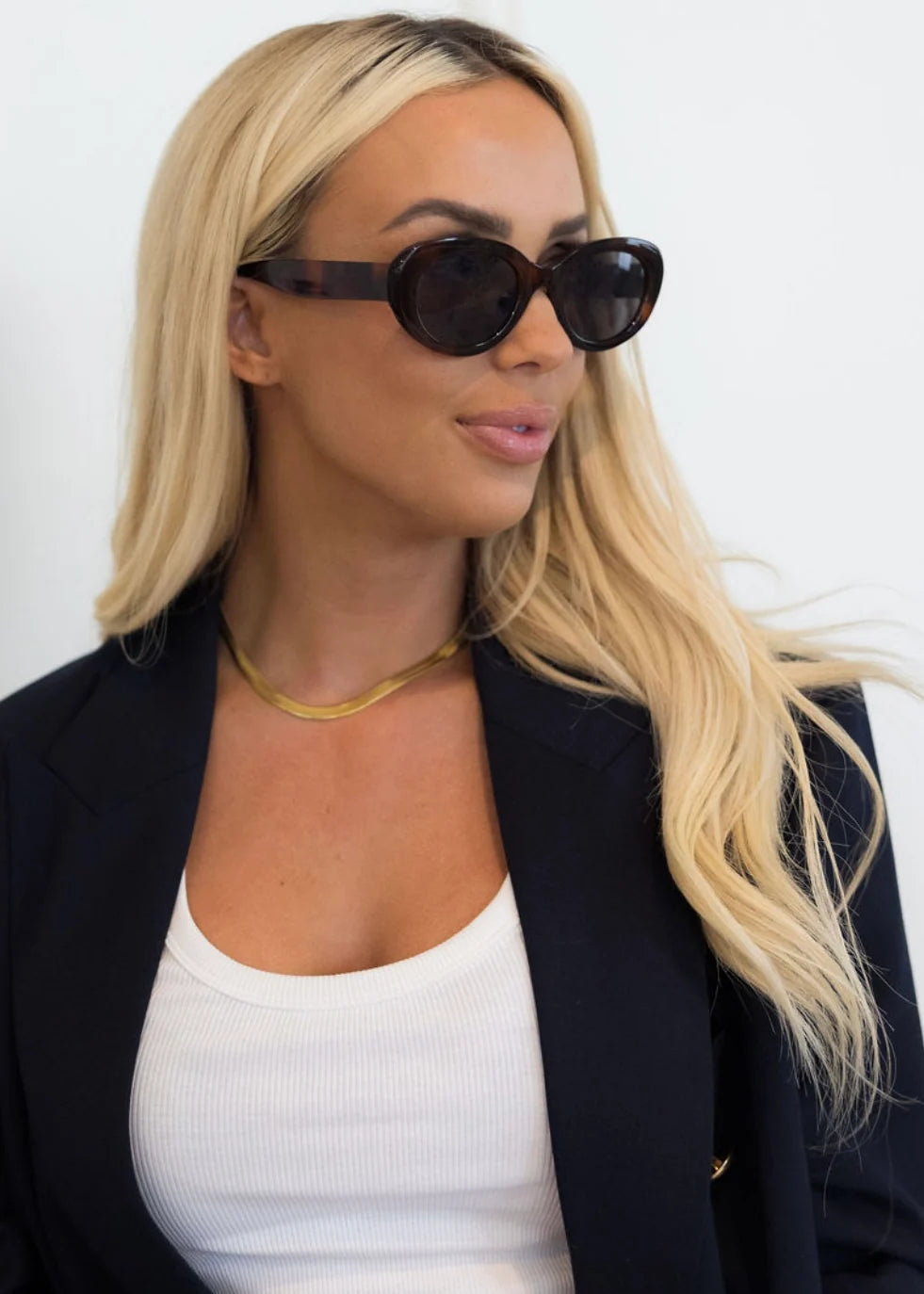 Woman wearing black jacket and white shirt with gold chain necklace