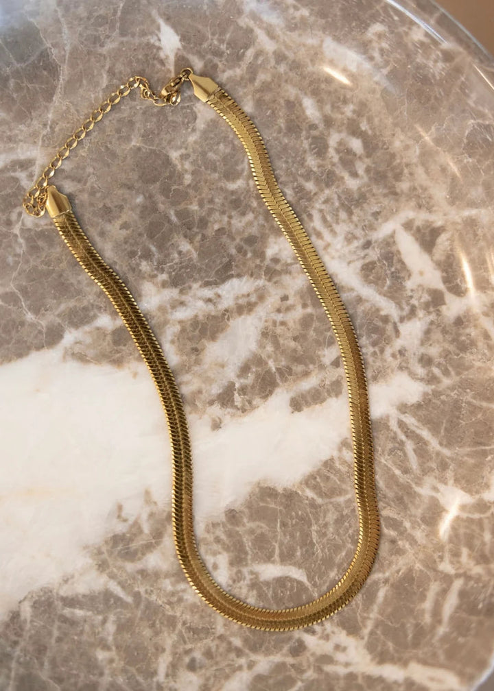 Gold herringbone chain on marble slab