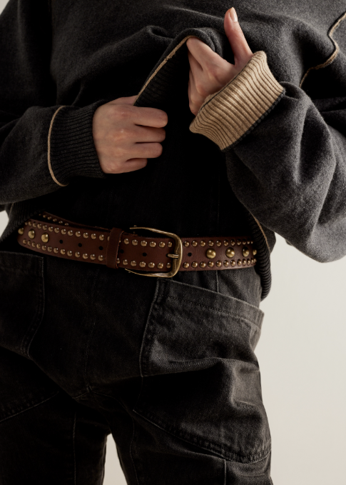 Woman wearing black sweatshirt and pants with brown studded belt on plain background