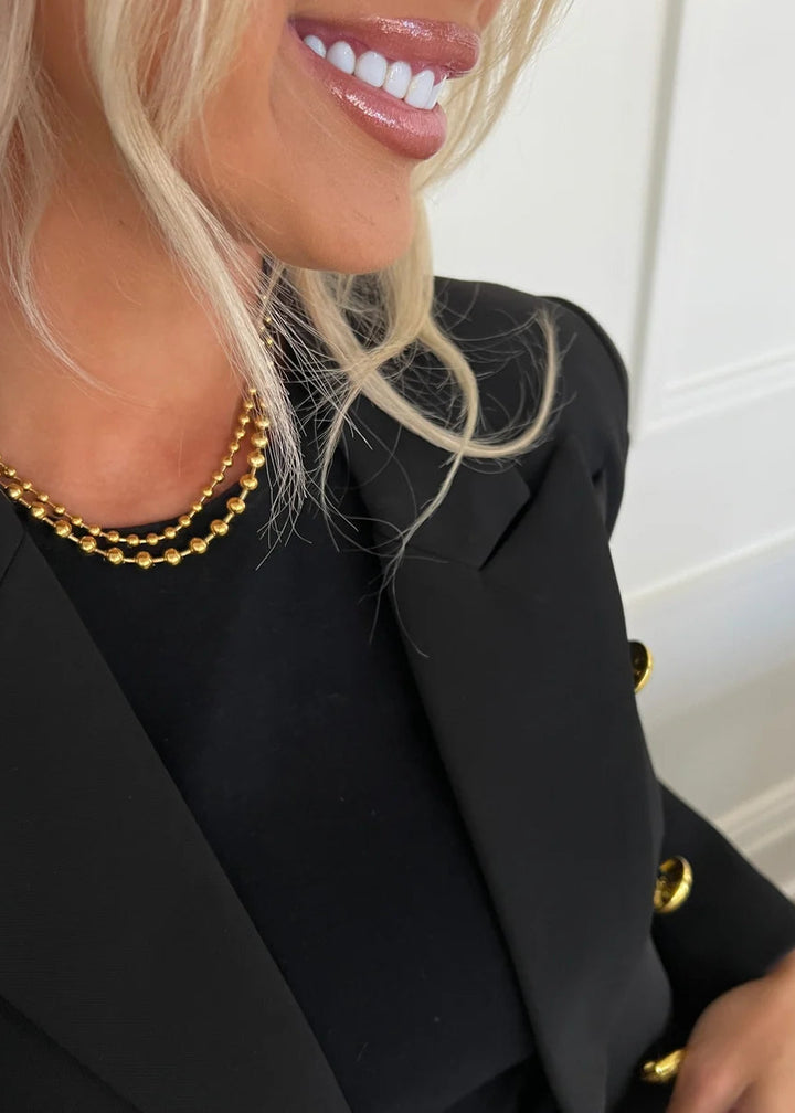 Person wearing a black blazer with gold buttons and a gold necklace.