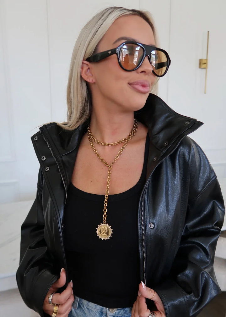 Woman wearing a black leather jacket, black top, and sunglasses indoors.