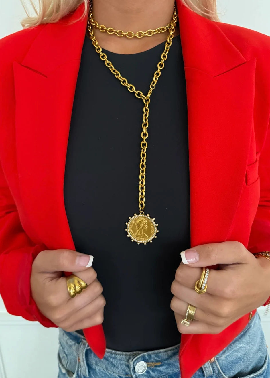 Person wearing a red blazer, black top, and gold chain necklace with a pendant.