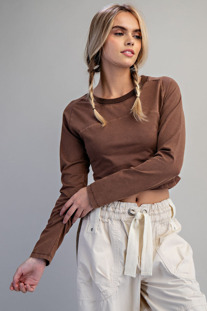 A woman modeling a brown long-sleeve crop top paired with cream cargo pants against a solid gray studio background.