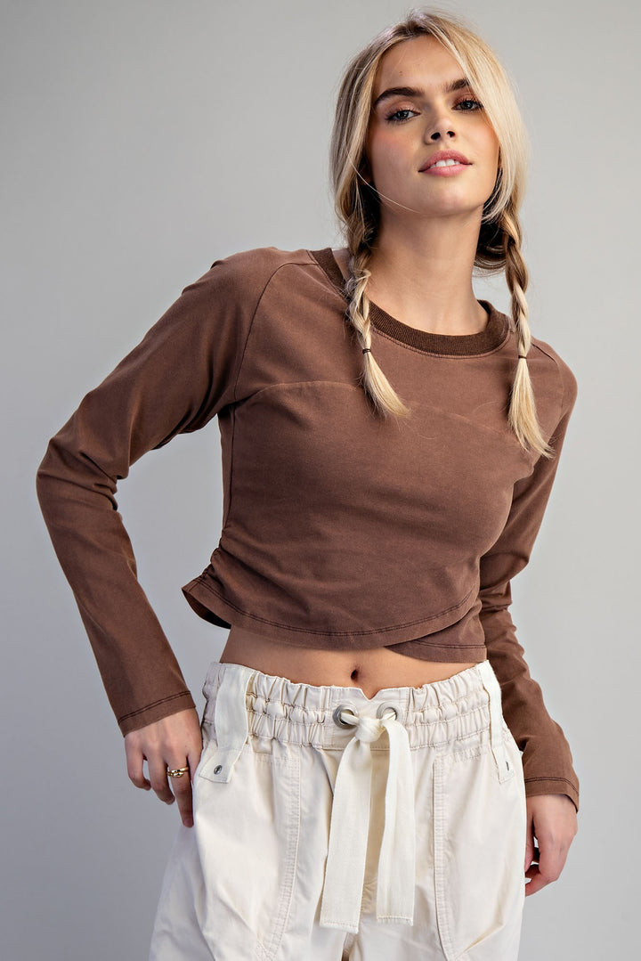 A blonde model with braided hair wearing a brown long-sleeve crop top and cream drawstring pants, photographed against a solid gray studio background.