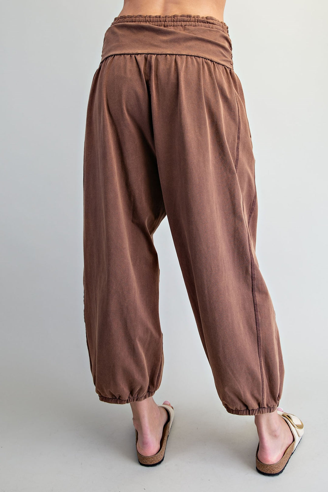 Rust brown harem-style pants with an elastic waistband and gathered ankle cuffs, shown on a model from the back against a light gray studio background.