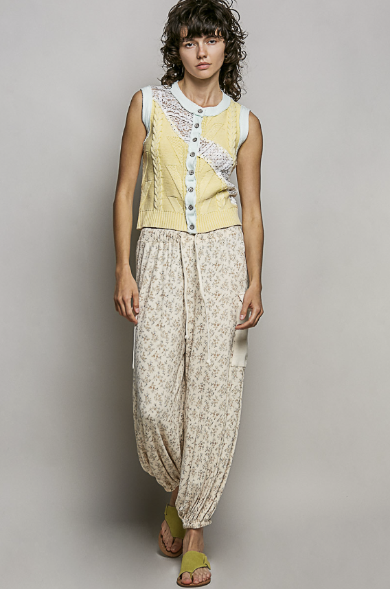 Woman wearing a sleeveless top with lace details and patterned pants against a plain background