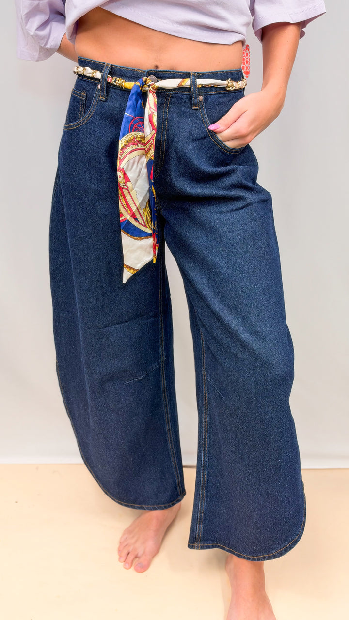 Woman wearing dark tulip hem jeans with purple tee on plain background