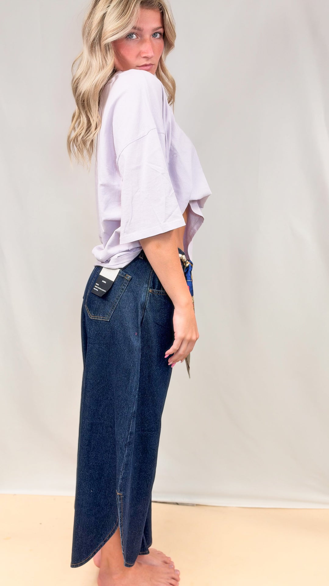 Woman wearing dark tulip hem jeans with purple tee on plain background