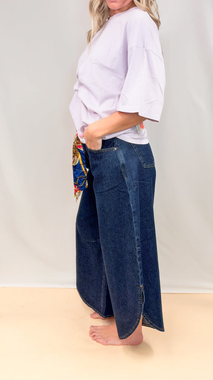 Woman wearing dark tulip hem pants with purple tee on plain background