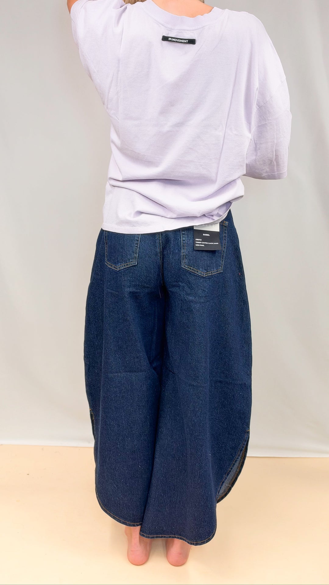 Woman wearing dark tulip hem jeans with purple tee on plain background