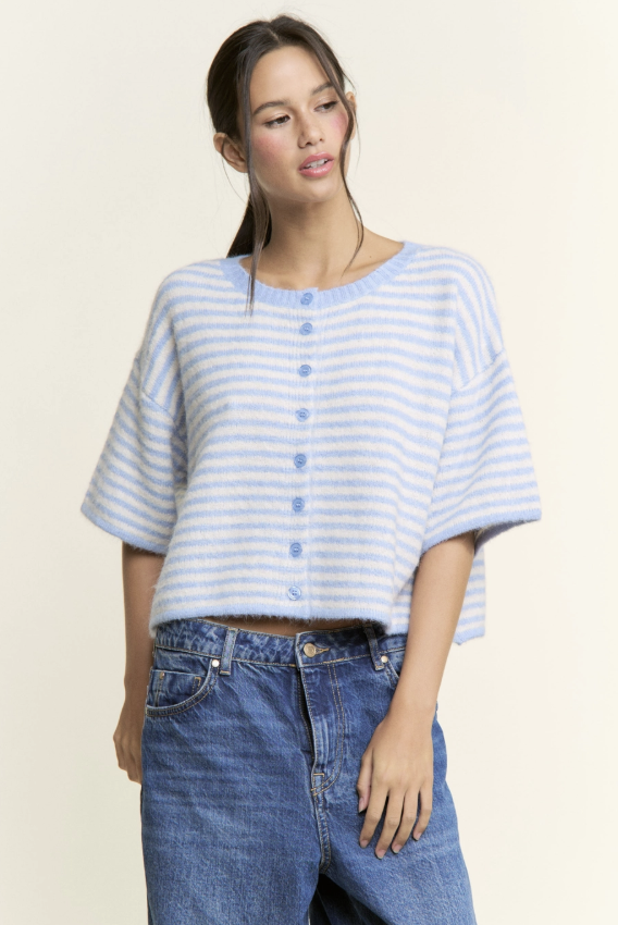 Woman wearing a light blue and white striped shirt with rolled-up sleeves and blue jeans on a beige background
