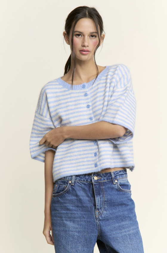 Woman wearing a light blue and white striped shirt with rolled-up sleeves and blue jeans on a beige background