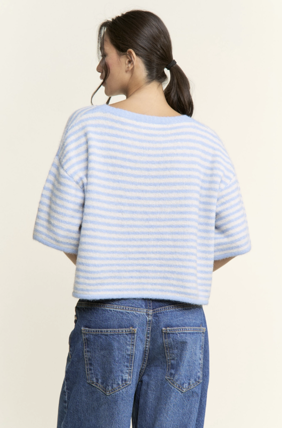 Person wearing a light blue and white striped shirt and blue jeans on a beige background