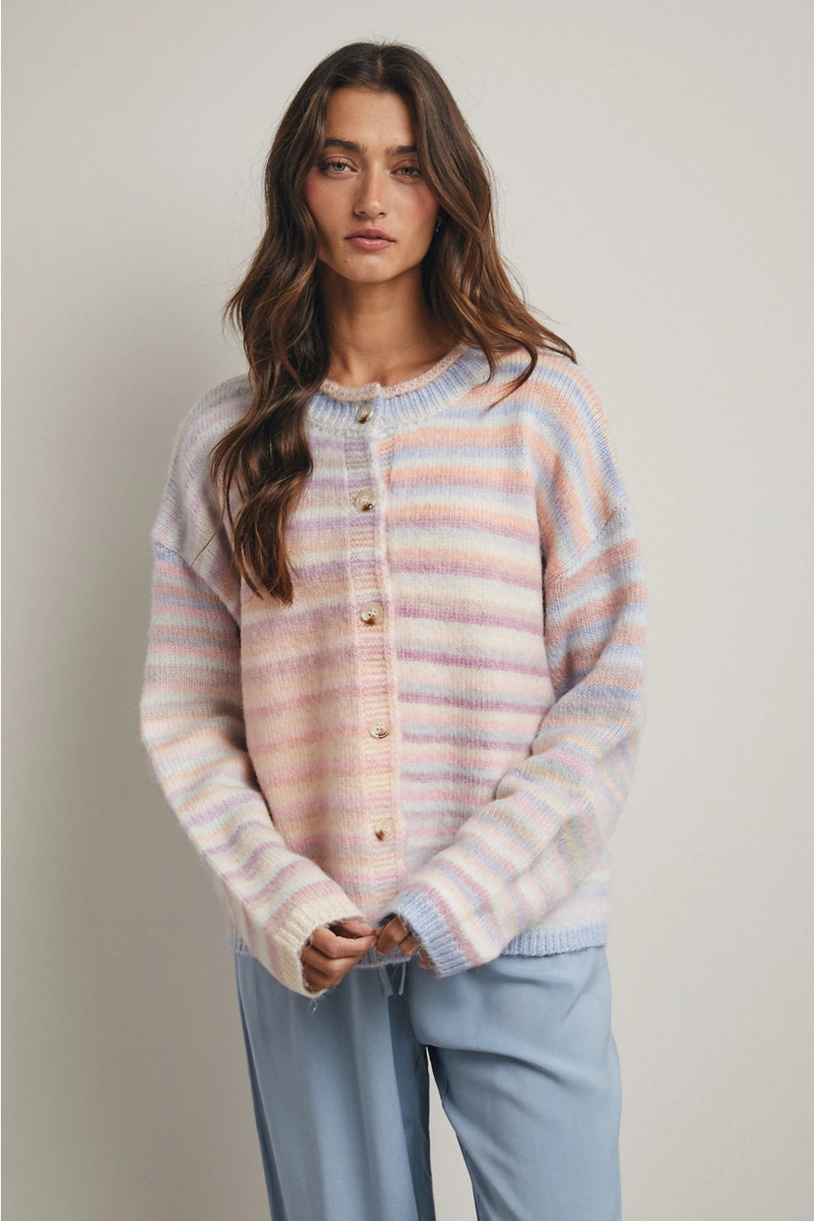 Woman wearing pastel striped cardigan and blue pants on plain background