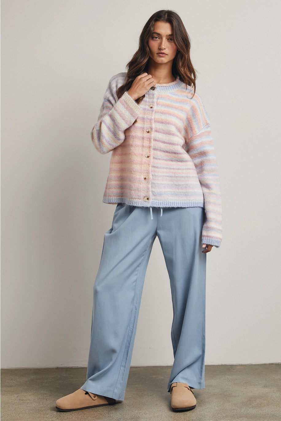 Woman wearing pastel striped cardigan and blue pants on plain background