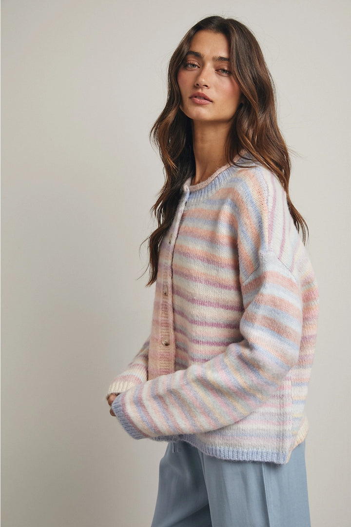 Woman wearing pastel striped cardigan and blue pants on plain background