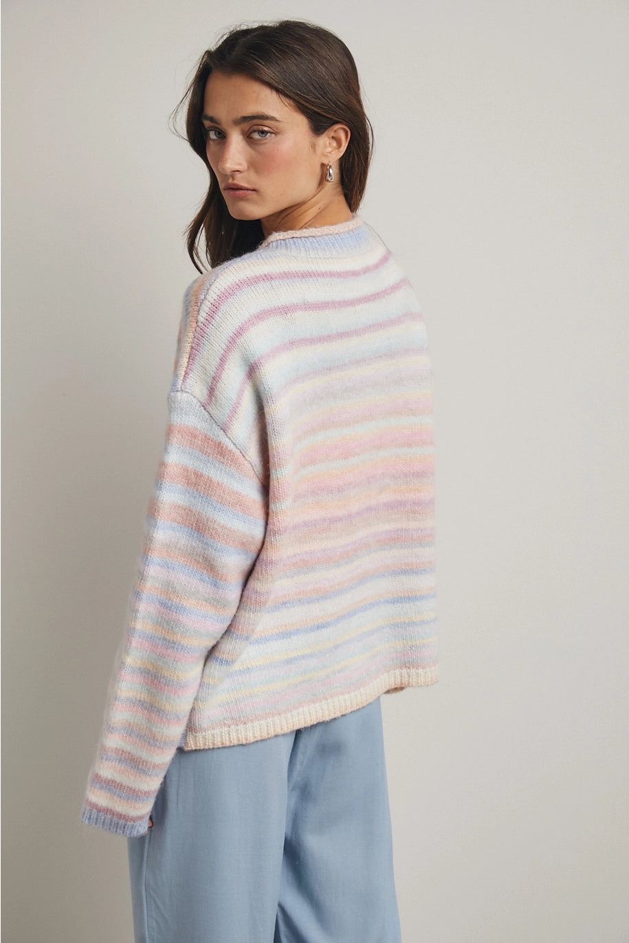 Woman wearing pastel striped cardigan and blue pants on plain background