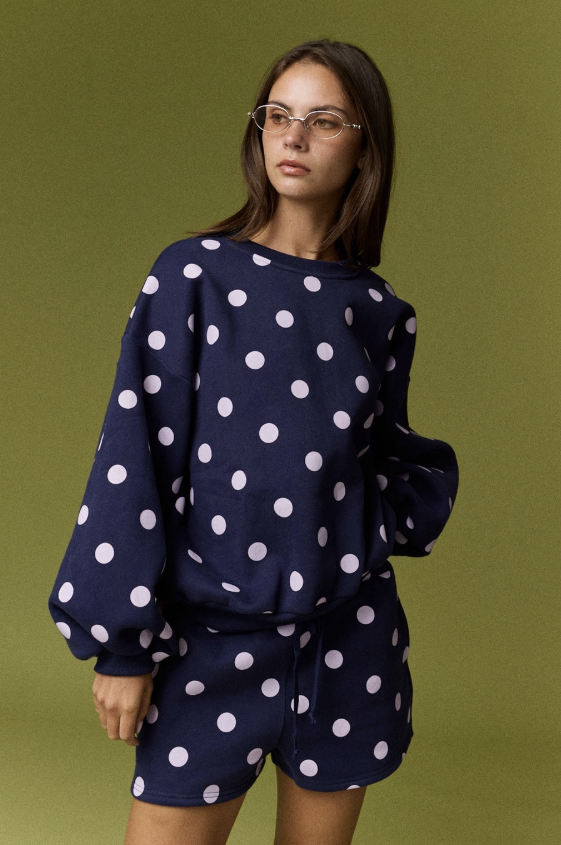 Woman wearing matching set that is navy with lilac dots on green background