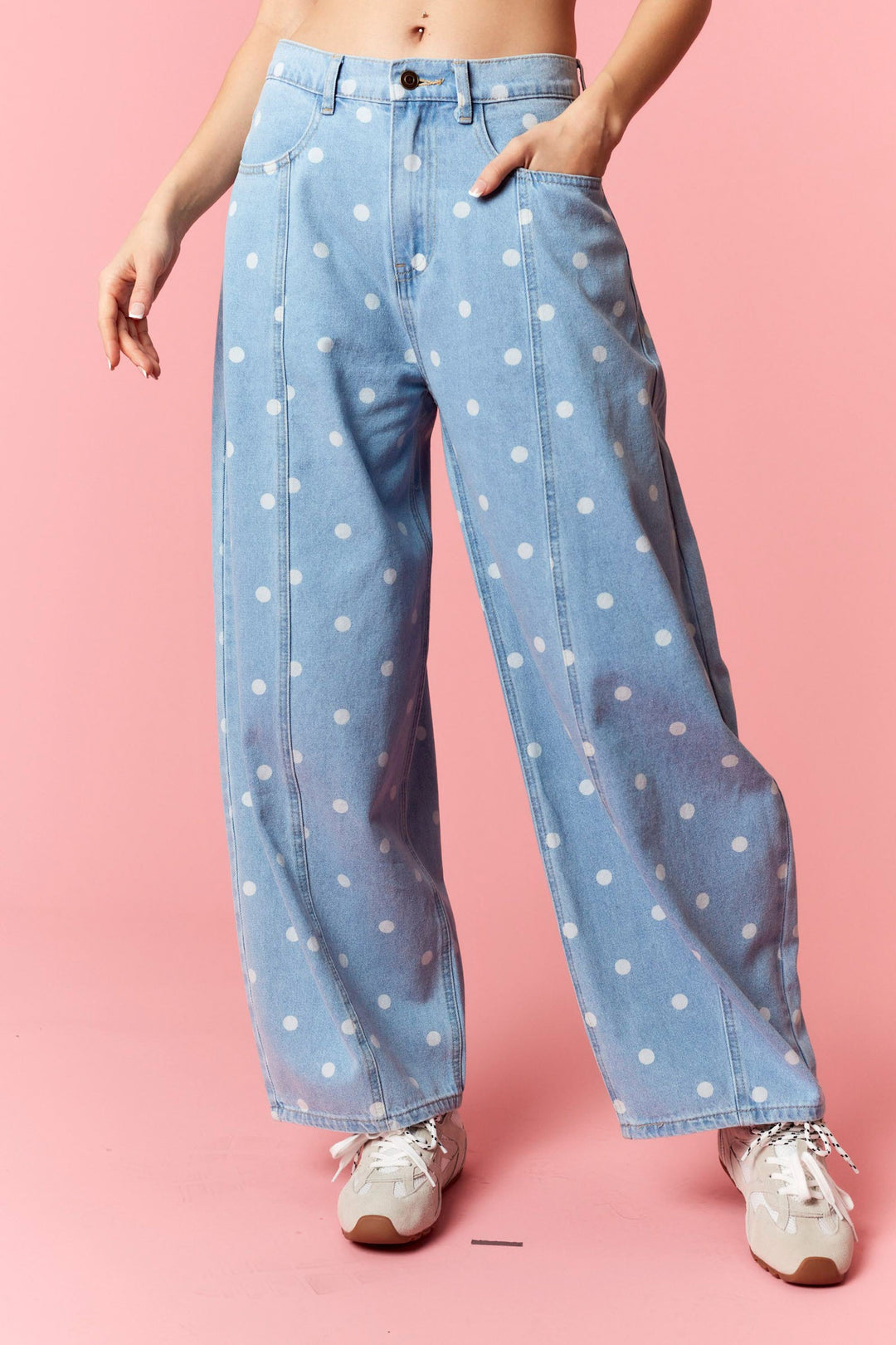 Person wearing light blue jeans with white polka dots on a pink background