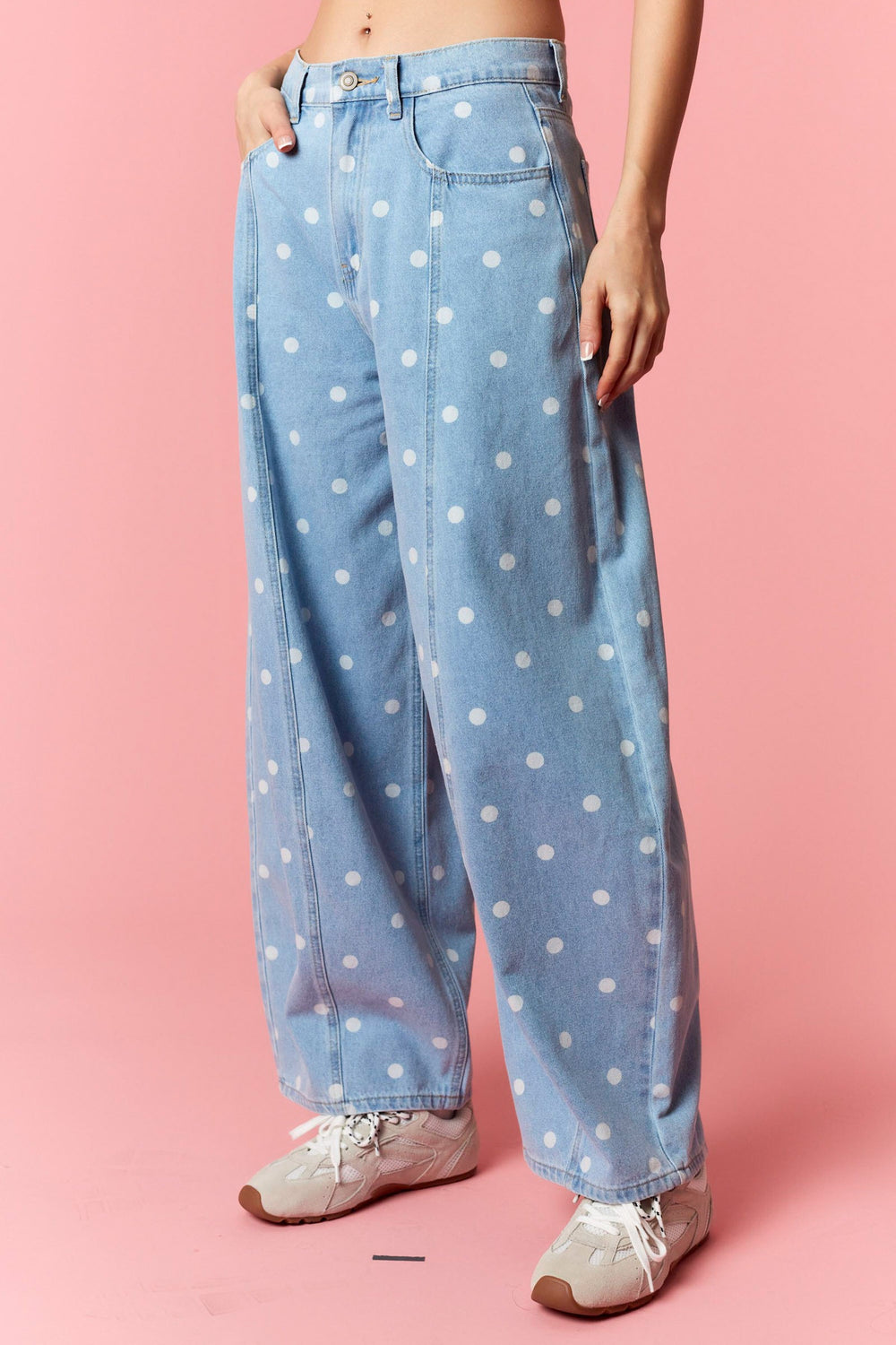 Light blue jeans with white polka dots worn by a person on a pink background
