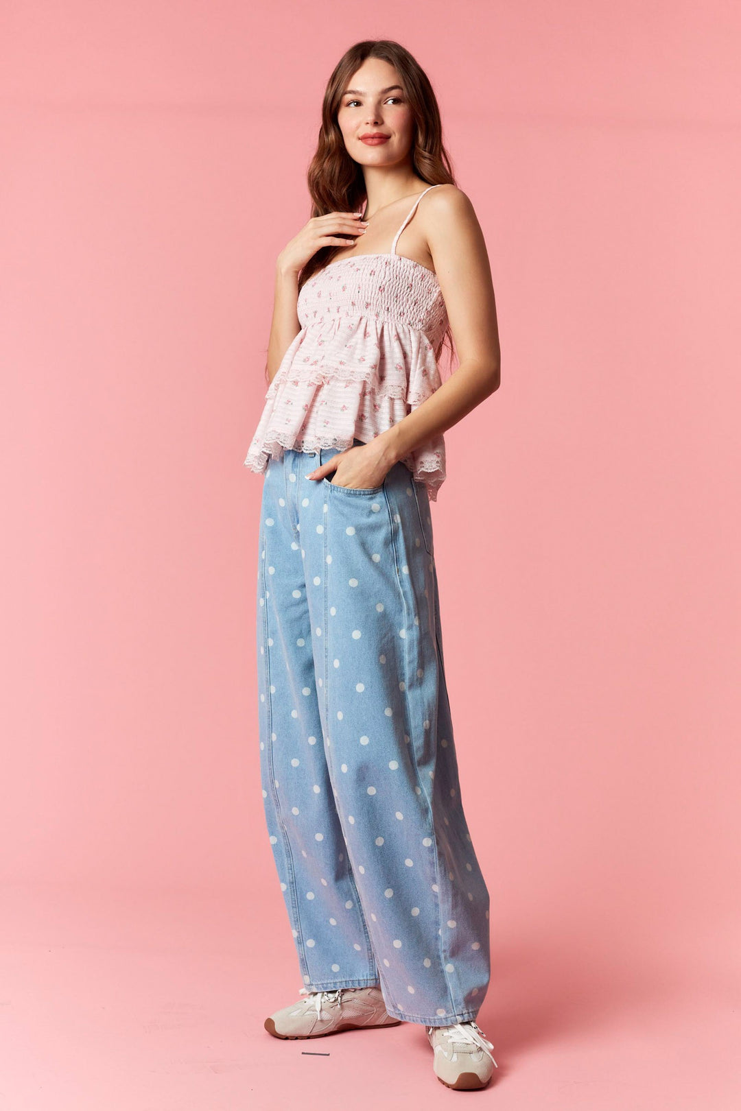 Woman wearing a pink top and blue polka dot pants on a pink background